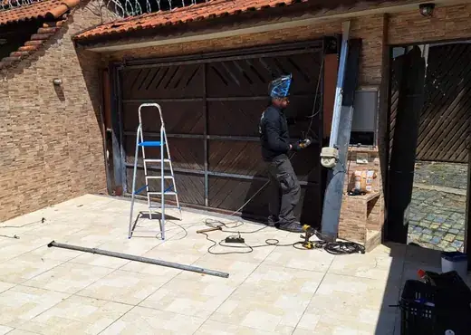 Técnico da LCA soldando um portão basculante de madeira com motor em uma casa de Guarulhos